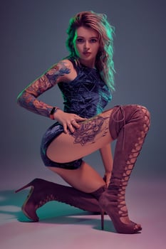 Attractive young blonde girl in blue velour booty shorts and maroon suede high boots posing on camera in studio photo