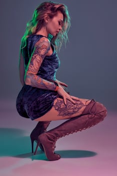Attractive young blonde girl in blue velour booty shorts and maroon suede high boots posing on camera in studio photo