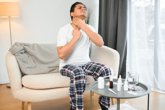 Sick young indian man suffering throat ache while sitting on bed at home photo