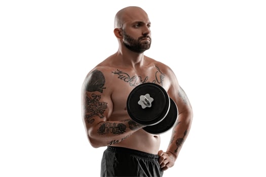 Athletic bald, tattooed man in black shorts is posing with a dumbbell isolated on white background. Close-up portrait. photo