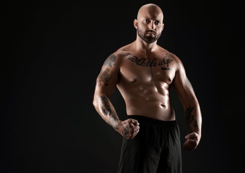 Athletic bald, bearded, tattooed man in black shorts is posing against a black background. Close-up portrait. photo