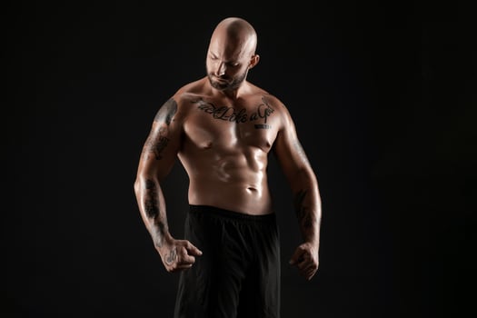 Athletic bald, bearded, tattooed man in black shorts is posing against a black background. Close-up portrait. photo