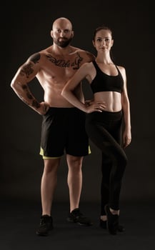 Athletic man in shorts and sneakers with brunette woman in leggings and top posing on black background. Fitness couple, gym concept. photo