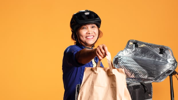Close up shot of courier arriving to customer address, taking meal bag out of thermic backpack. Happy BIPOC bike rider delivering lunch to client, isolated over studio background photo