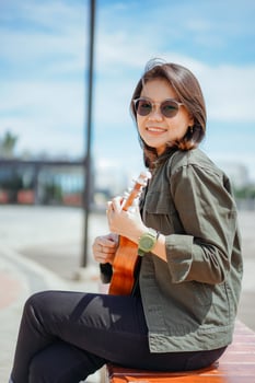 Playing Ukulele of Young Beautiful Asian Woman Wearing Jacket And Black Jeans Posing Outdoors photo