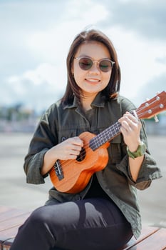 Playing Ukulele of Young Beautiful Asian Woman Wearing Jacket And Black Jeans Posing Outdoors photo