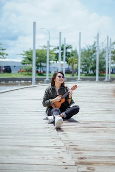 Playing Ukulele of Young Beautiful Asian Woman Wearing Jacket And Black Jeans Posing Outdoors photo