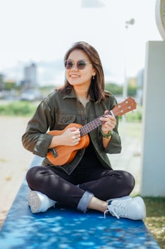 Playing Ukulele of Young Beautiful Asian Woman Wearing Jacket And Black Jeans Posing Outdoors photo
