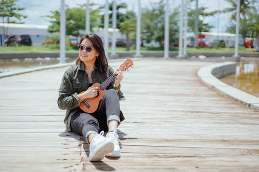 Playing Ukulele of Young Beautiful Asian Woman Wearing Jacket And Black Jeans Posing Outdoors photo