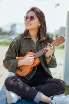 Playing Ukulele of Young Beautiful Asian Woman Wearing Jacket And Black Jeans Posing Outdoors photo