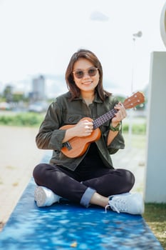 Playing Ukulele of Young Beautiful Asian Woman Wearing Jacket And Black Jeans Posing Outdoors photo