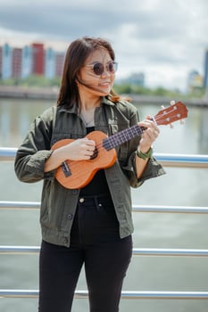 Playing Ukulele of Young Beautiful Asian Woman Wearing Jacket And Black Jeans Posing Outdoors photo