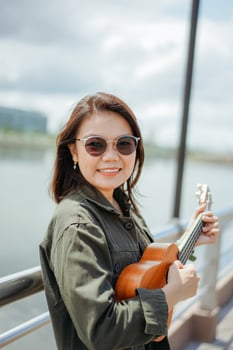 Playing Ukulele of Young Beautiful Asian Woman Wearing Jacket And Black Jeans Posing Outdoors photo