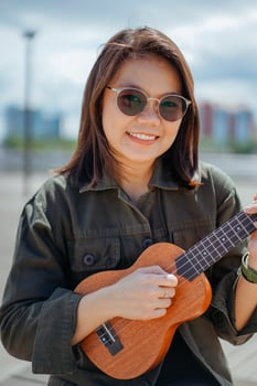 Playing Ukulele of Young Beautiful Asian Woman Wearing Jacket And Black Jeans Posing Outdoors photo