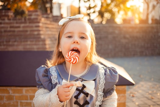 beautiful little girl eats, licks with tongue delicious candy, dressed as witch, outdoors, fall, October 31, Happy Halloween. Portrait funny. photo