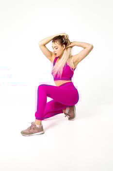 Woman in vibrant pink sports outfit kneeling with hands on hairs photo