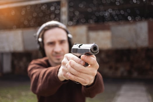 A man shoots a gun, aiming at the target. A man wearing protective headphones. A wall and a roof with bullet holes. outdoor shooting range photo