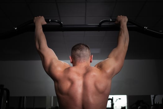 A man athlete bodybuilder pulls up on his hands, builds muscles, does an exercise in gym. photo