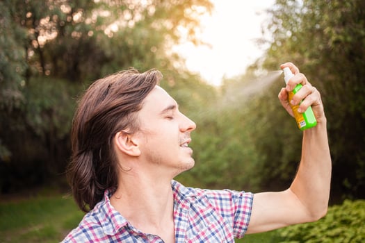 Young man spraying mosquito insect repellent in the forrest, protection. A man sprays mosquito spray on his face. photo