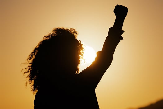 AI generated silhouette of a woman with flowing hair with her fist raised up in the sunset sky, girl power photo