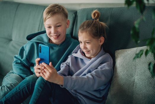 two children sitting on a couch looking at a phone photo