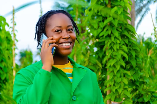 pretty african woman in the farm making calls in the farm while holding money on her other hand photo
