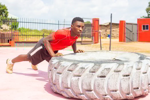 Strong sporty guy flipping workout wheel at outside gym photo