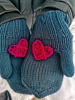 Close-up two hand-made of braided crimson colored hearts in men's hands dressed in winter blue knitted mittens photo