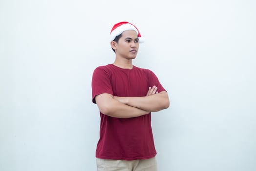 Young Asian man wearing a Santa Claus hat crossing his arms while smiling, shock and laughing with a white background for visual communication photo