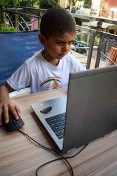 Little boy sitting at table using laptop for online class in Grade 1, Child studying on laptop from home for distance learning online education, School boy children lifestyle concept photo