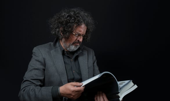Man with white beard and black curly hair reading a book, wearing black shirt against black background photo