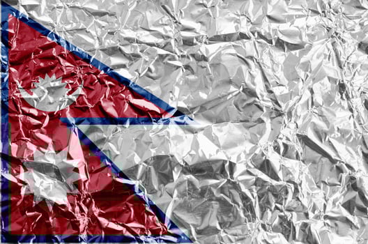 Nepal flag depicted in paint colors on shiny crumpled aluminium foil closeup. Textured banner on rough background photo