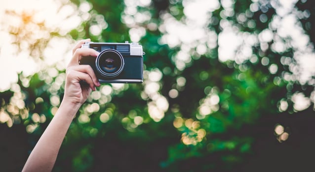 The hand that is holding up holds the old camera to take a picture. photo