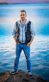 Man Standing on Rock by the Water. A man standing on top of a rock next to a body of water photo