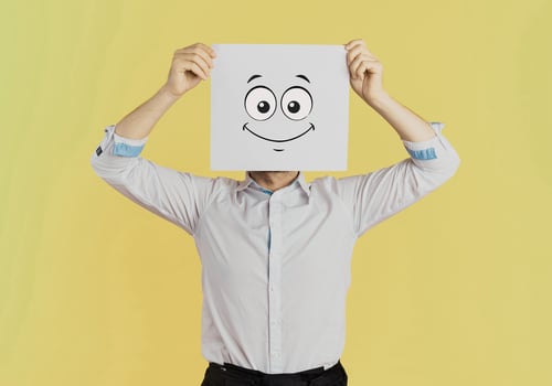 Young businessman holding white card with a happy face on it isolated on Yellow background photo