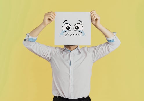 Young businessman holding white card with a sad face on it isolated on Yellow background photo