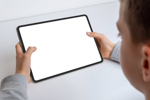Close-up of a boy's hands holding a tablet mockup. Engaged in work, showcasing an isolated white screen for app presentation. Modern technology in kid hands photo