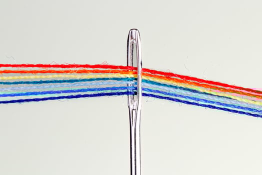 multi-colored threads for sewing in the form of a rainbow pass through an antique needle on a white background photo