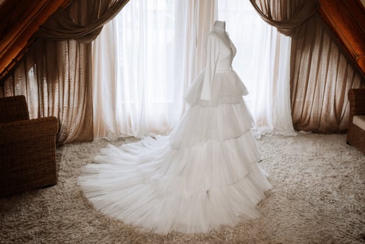 A white wedding dress with a train on a mannequin in a hotel room against a window background photo