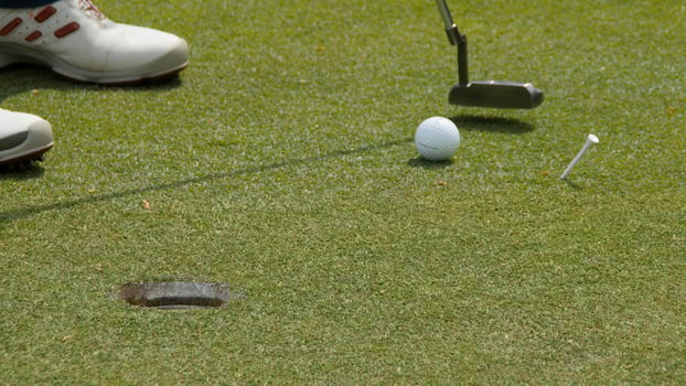 Professional golfer putting ball into the hole. Golf ball by the edge of hole with player in background on a sunny day. photo