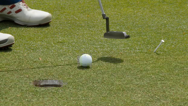Professional golfer putting ball into the hole. Golf ball by the edge of hole with player in background on a sunny day. photo