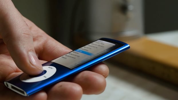Music player in male hand, on home interior background. Toggles the music on the player close up photo