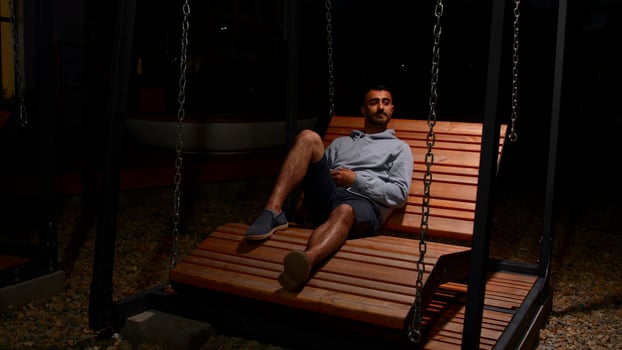 A man resting in the night. Media. An adult cute brunette in shorts who sits on a bench at night. photo