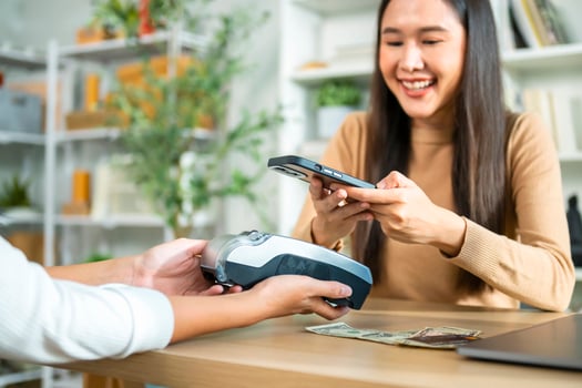 Young Asian woman smiling and paying with smartphone in restaurant photo