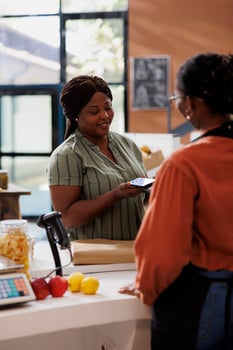 An African American vendor smiles as a customer uses contactless payment at a bio food market. Freshly harvested, organic produce is available for sale. photo