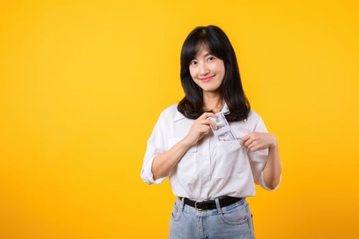 Captivating image of Asian young woman wearing white shirt and denim jeans, confidently holding cash from her shirt pocket. Fashion meets financial empowerment. Perfect for finance and fashion themes. photo