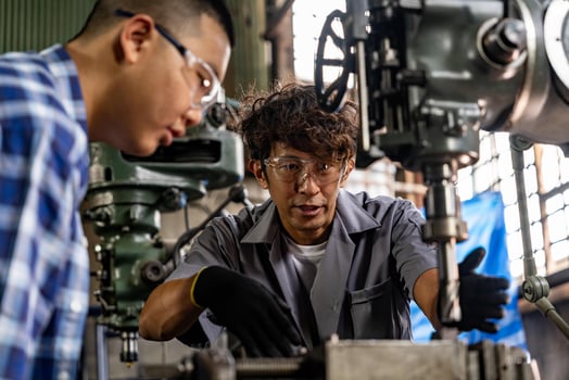 Asian worker in production plant drilling at machine. Professional worker near drilling machine on factory. finishing metal working internal steel surface on lathe grinder machine with flying sparks. photo