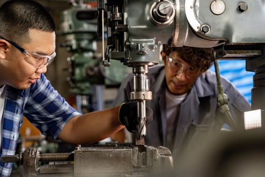 Asian worker in production plant drilling at machine. Professional worker near drilling machine on factory. finishing metal working internal steel surface on lathe grinder machine with flying sparks. photo