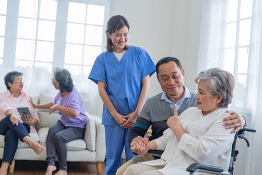 A young Asian nurse helps an elderly couple, the man sitting in a wheelchair, at a care center. photo