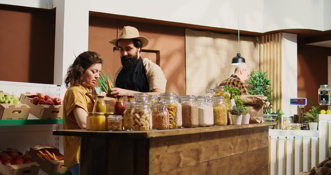 Client using paper bag in chemicals free food supermarket, inquiring about products ethical sourcing. Woman in local store using renewable energy chatting with trader about pantry staples photo